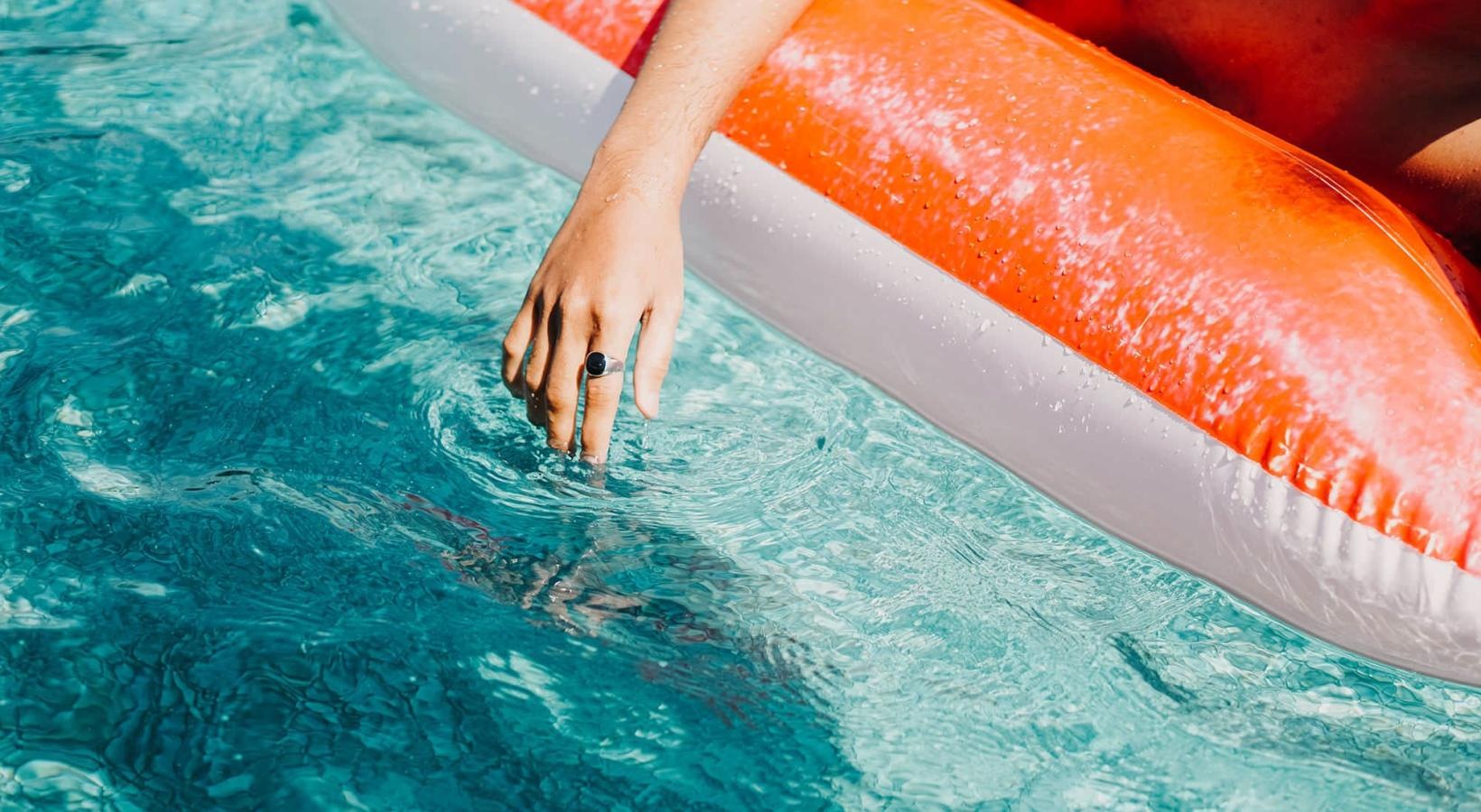 Resort-style swimming pool woman dangles her hand in the pool as she floats in an inflatable vessel